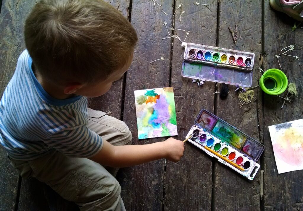 Young boy watercolors on paper on the deck of West Fork Cabin.