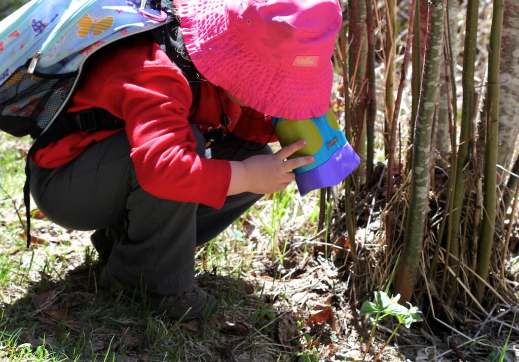 Young girl looks at at trillium through binoculars.