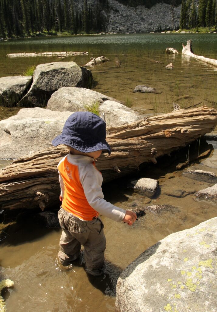 Toddler boy explores lake shore by wading in shallow water.