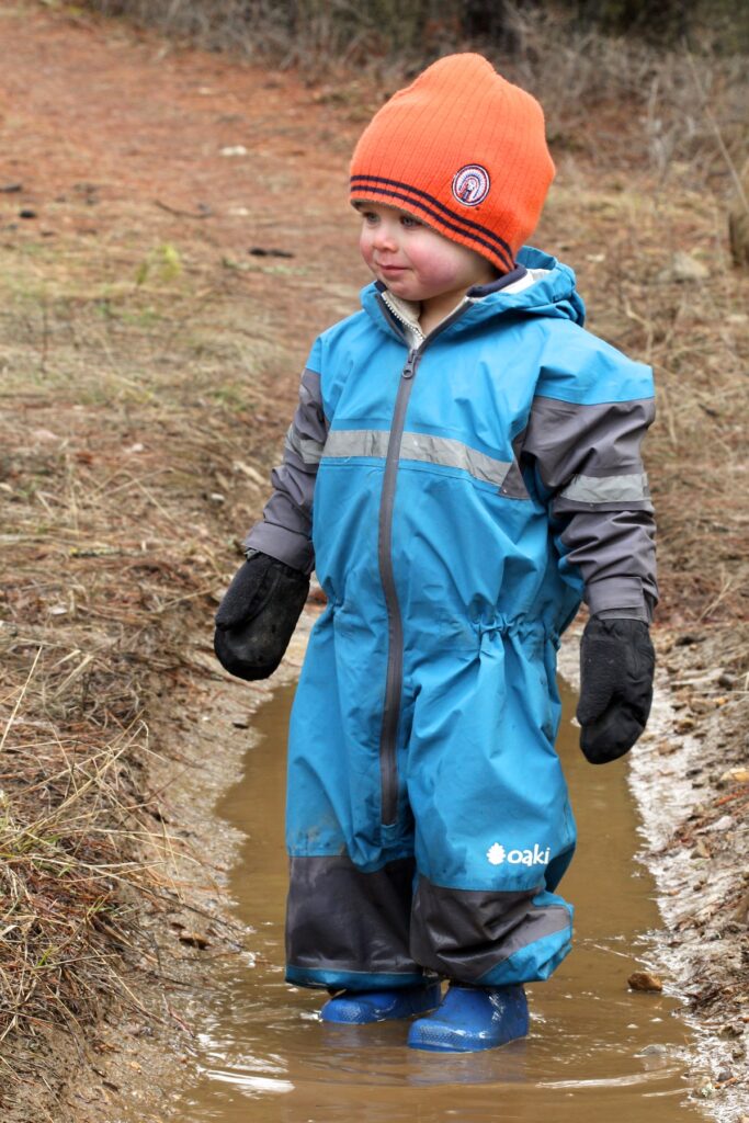 Toddler wearing rain suit standing in mud puddle.