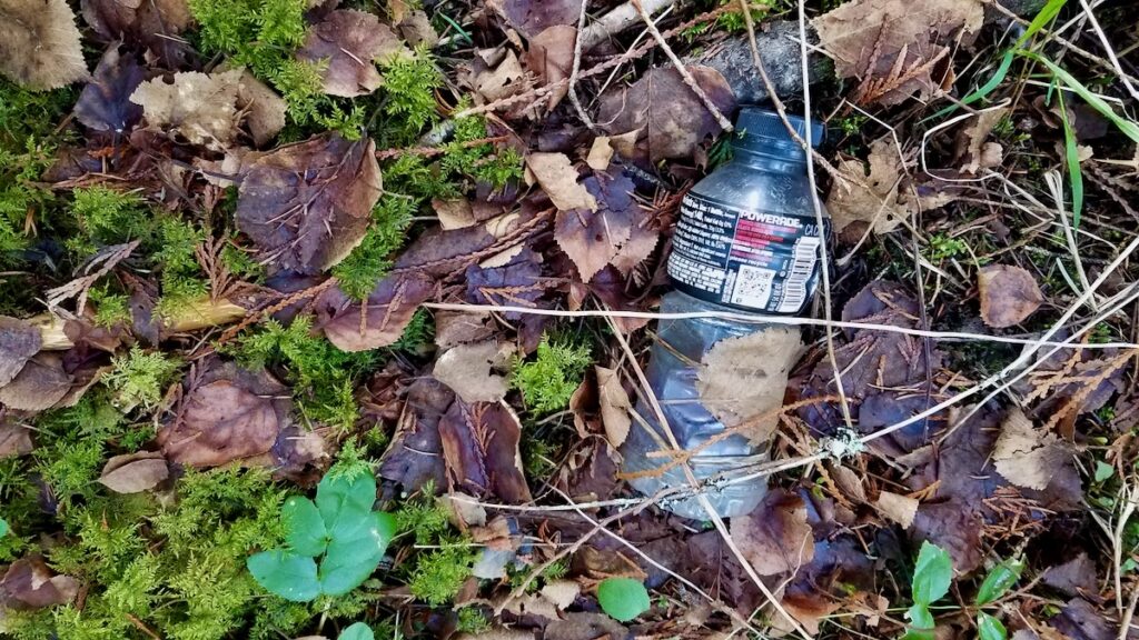 Plastic sports drink bottle laying in the woods.